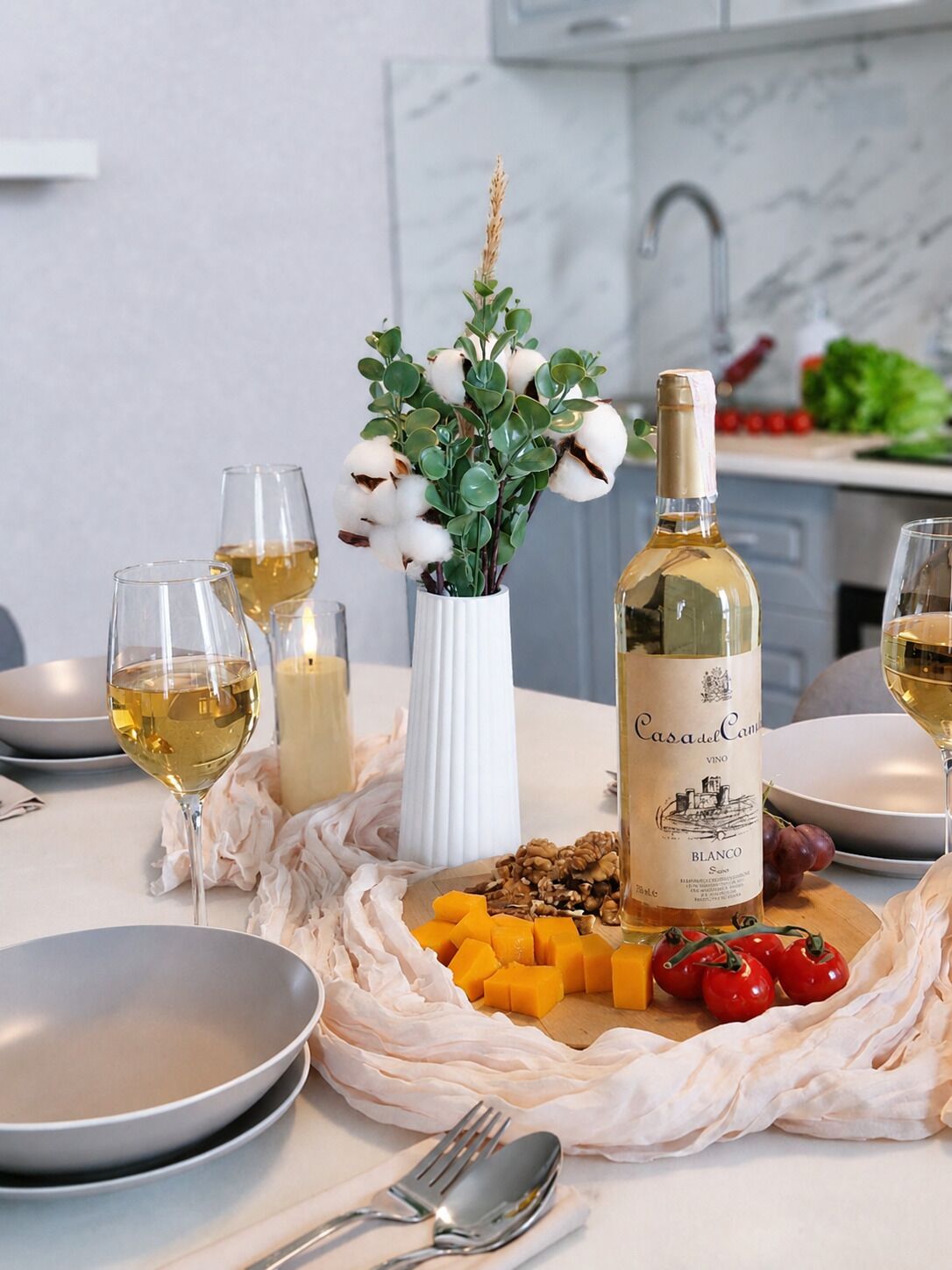 A dining table with a bottle of wine, glasses, a vase with flowers, and a plate with food.