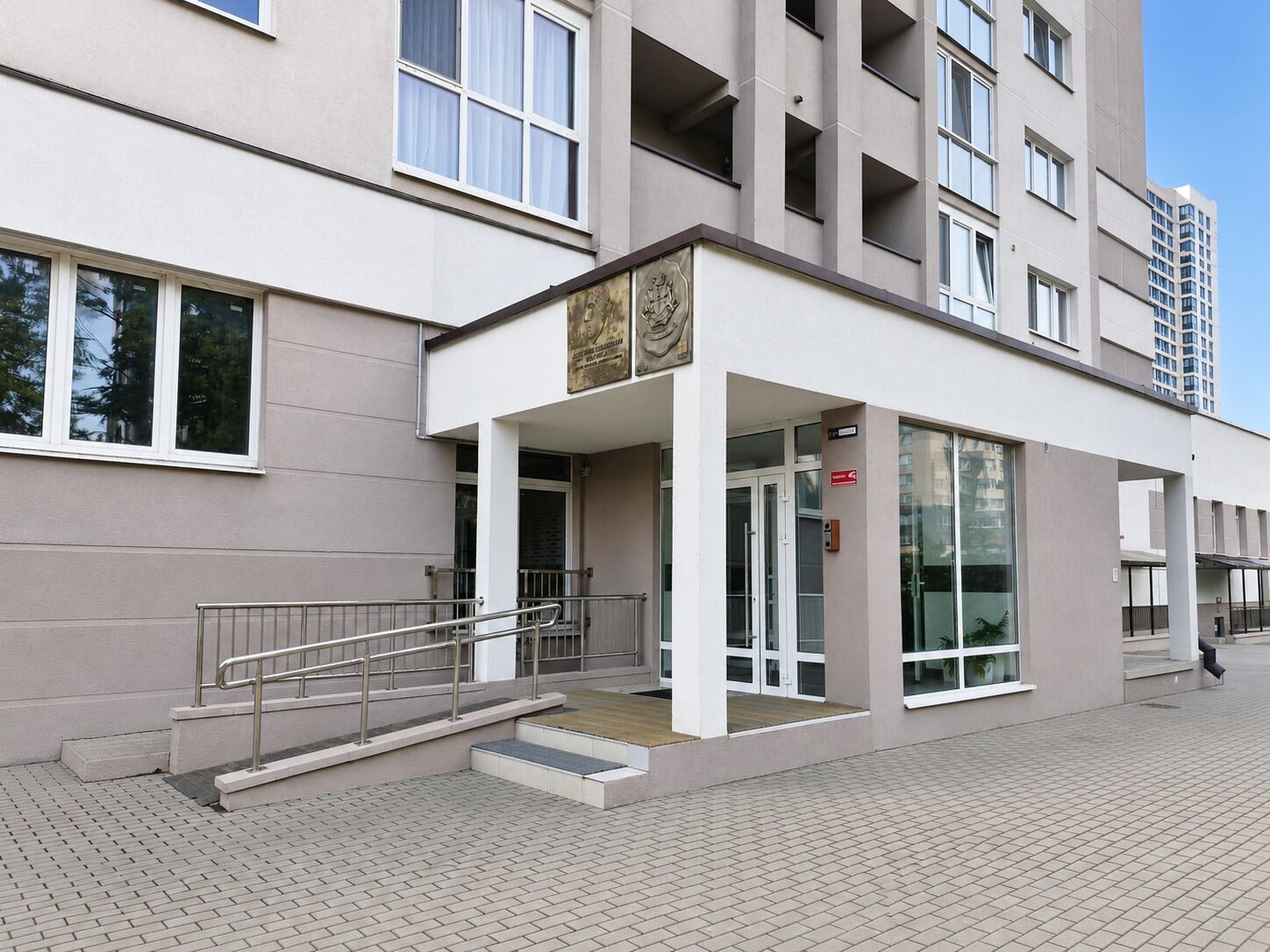 Un edificio moderno con fachada plana, ventanas amplias y una entrada destacada con una escalera de metal que conduce a una plataforma de madera.