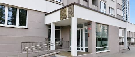 Un edificio moderno con fachada plana, ventanas amplias y una entrada destacada con una escalera de metal que conduce a una plataforma de madera.