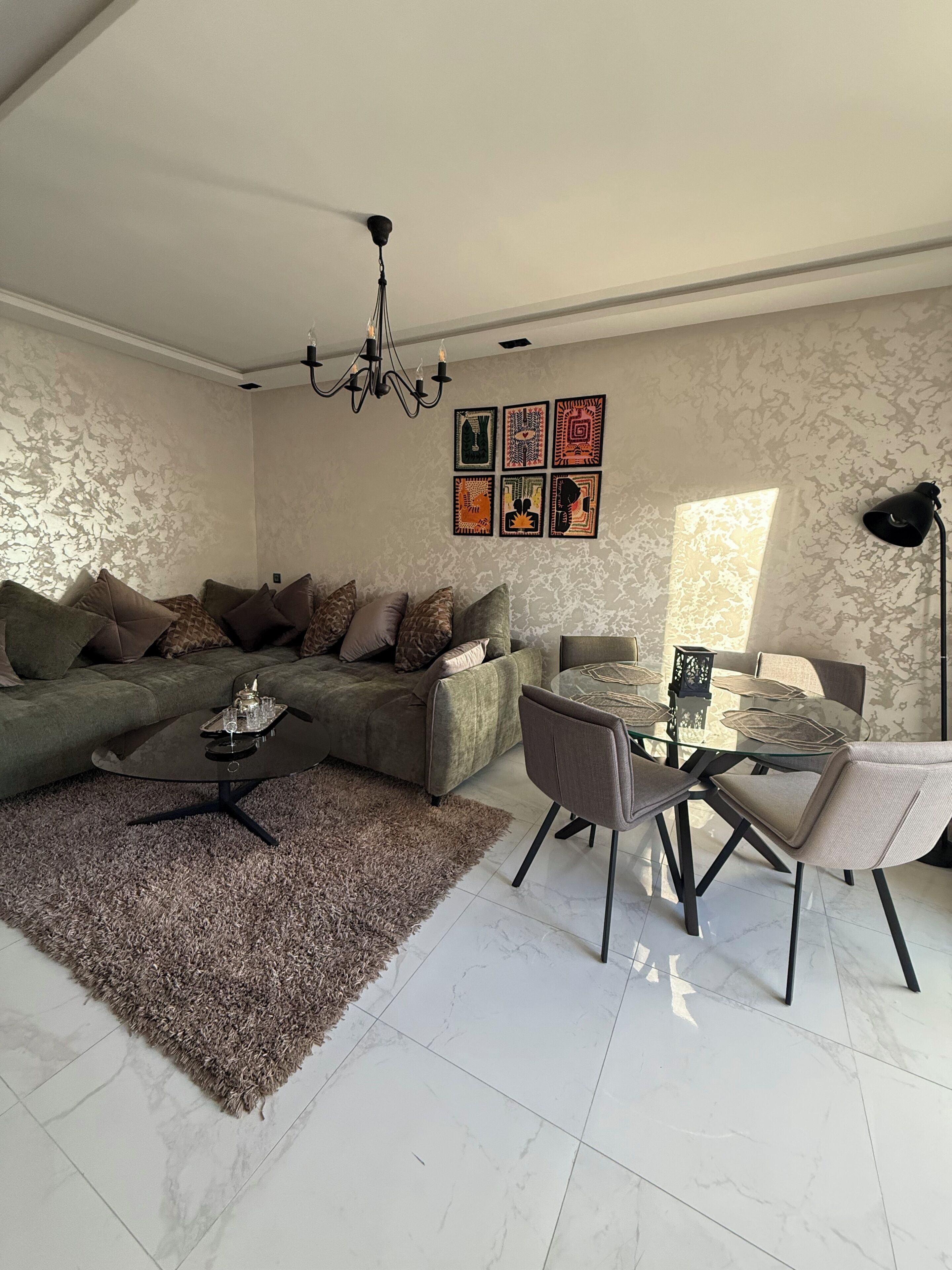 A living room with a sofa, coffee table, dining table, chairs, a chandelier, wall art, and a lamp.