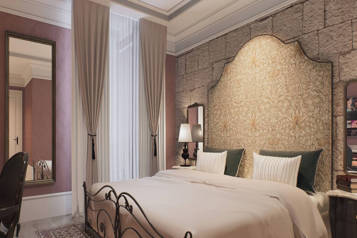 A bedroom with a large bed, a desk, a chair, a mirror, and a patterned wall.