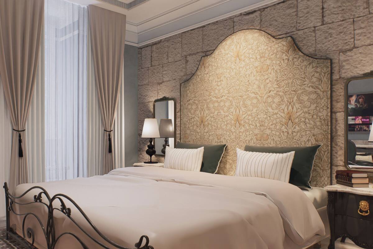A bedroom with a large bed, a nightstand, a lamp, a mirror, and a stone-patterned wall.