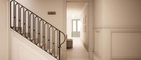 Un pasillo con una escalera, una puerta al final y un letrero con un número en la pared.