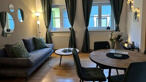 Un salon comprenant un canapé, une table basse ronde, une table à manger avec des chaises et une fenêtre avec des rideaux.
