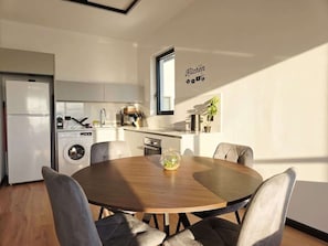 Eine moderne Küche mit integriertem Waschmaschine, einem Essbereich mit rundem Tisch und Stühlen sowie einem Schild mit der Aufschrift 'Kitchen'.