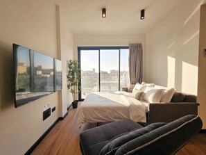 Ein modernes Schlafzimmer mit großem Fenster, einem Bett, einer Couch und einem Fernseher.