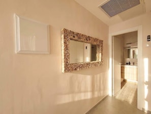 A hallway with a mirror framed by stacked logs, a white wall, and a door leading to a kitchen area.