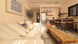 Ein modernes Wohnzimmer mit einer Couch, einer Holzbank und einer Küchenzeile im Hintergrund.