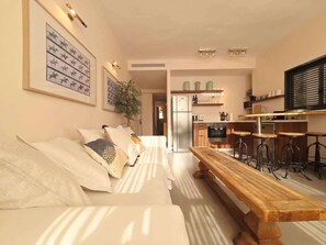 A modern living room with a sofa, a wooden bench, and a kitchen area in the background.