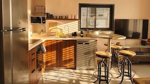 Eine moderne Küche mit Einbauofen, Mikrowelle und Geschirrspüler, ein großes Fenster mit Jalousien und eine Theke mit Sitzgelegenheiten.