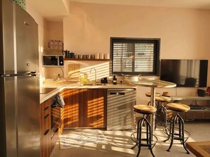 A modern kitchen with a built-in oven, microwave, and dishwasher, a large window with blinds, and a bar area with stools.