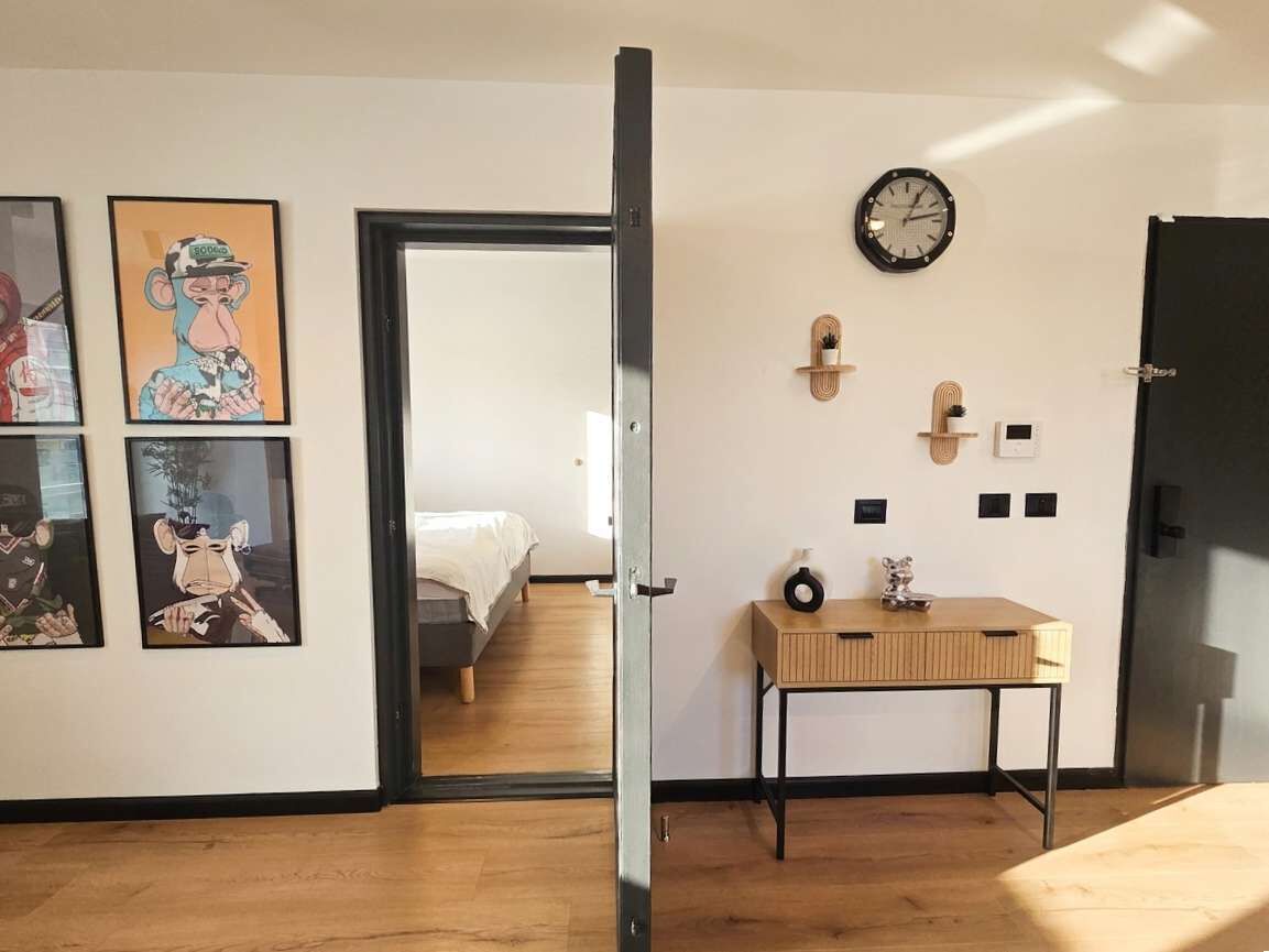 Quarto com cama, piso de madeira, escrivaninha com relógio e quadros na parede.