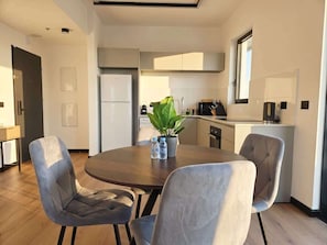 A modern kitchen with a dining area, including a round table, chairs, and a potted plant. - Herzl15 #TLV View- New 1BR & Mamad |By SweetyGuest (Tel Aviv-Yafo)