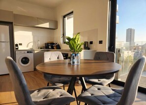 A modern kitchen with a washing machine, a dining table with chairs, and a large window with a city view. - Herzl15 #TLV View- New 1BR & Mamad |By SweetyGuest (Tel Aviv-Yafo)