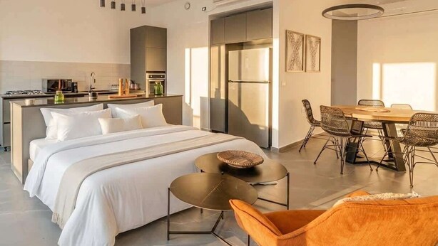 Ein modernes Hotelzimmer mit Bett, Essbereich, Küche und einem großen Fenster.