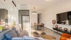 Ein modernes Wohnzimmer mit Sofa, Couchtisch, Essbereich und einem an der Wand befestigten Fernseher.