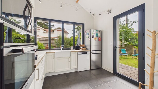 Una cocina moderna con armarios blancos, un refrigerador de acero inoxidable y ventanas amplias.