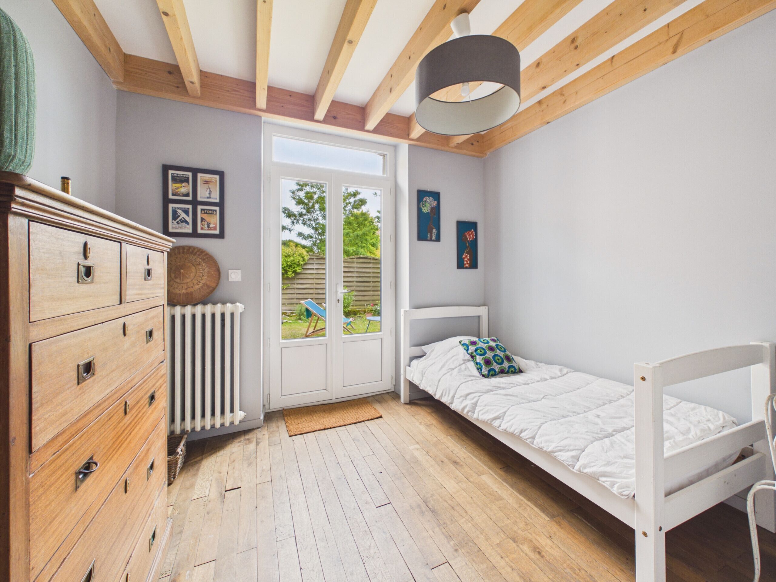 Ein Schlafzimmer mit einem hölzernen Schminktisch, einem Bett, einem Heizkörper und Blick durch eine Tür.