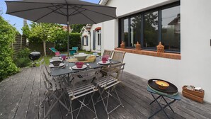 Un patio exterior con una mesa lista para comer, una parrilla y un paraguas grande.