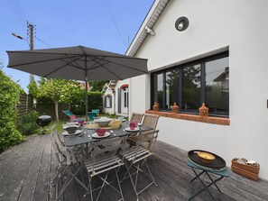 Eine Terrassengruppe mit Esstisch, Grill und großem Sonnenschirm.