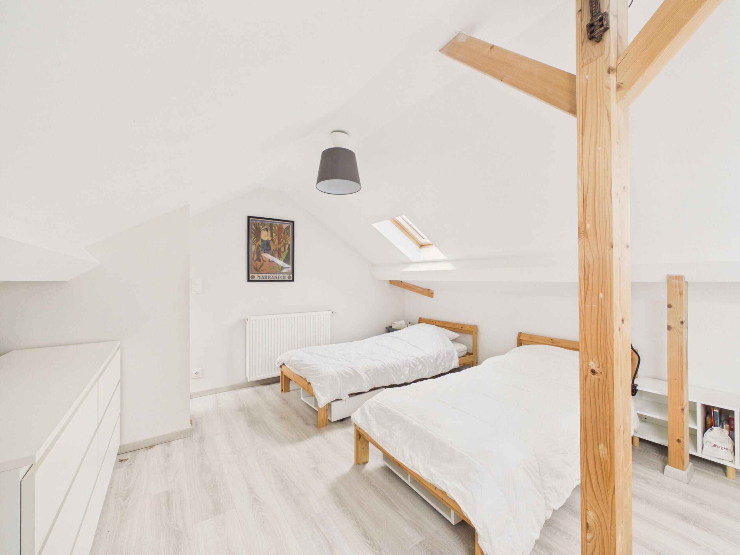 A bedroom with two beds, a radiator, a skylight, and a wooden ceiling structure.