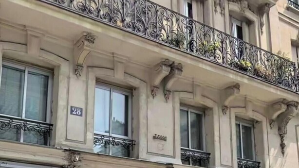 Un edificio de varios pisos con balcones ornamentados, una tienda en la planta baja y una puerta de madera grande.