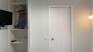 Habitación con una puerta blanca, un televisor montado en la pared y un perchero con una prenda colgada.