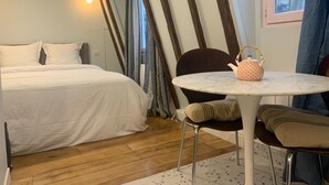 Un dormitorio con una cama, una mesita redonda con tetera, una silla y una ventana con cortinas.