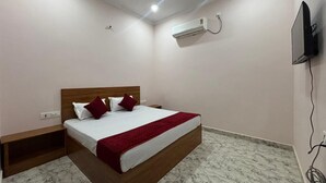 A bedroom with a bed, a nightstand, a TV, and an air conditioning unit. - Hotel Baldev Palace (Vrindavan)