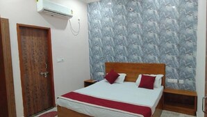 A bedroom with a wooden bed, a red and white bedspread, a patterned wallpaper, and a wooden wardrobe. - Hotel Baldev Palace (Vrindavan)