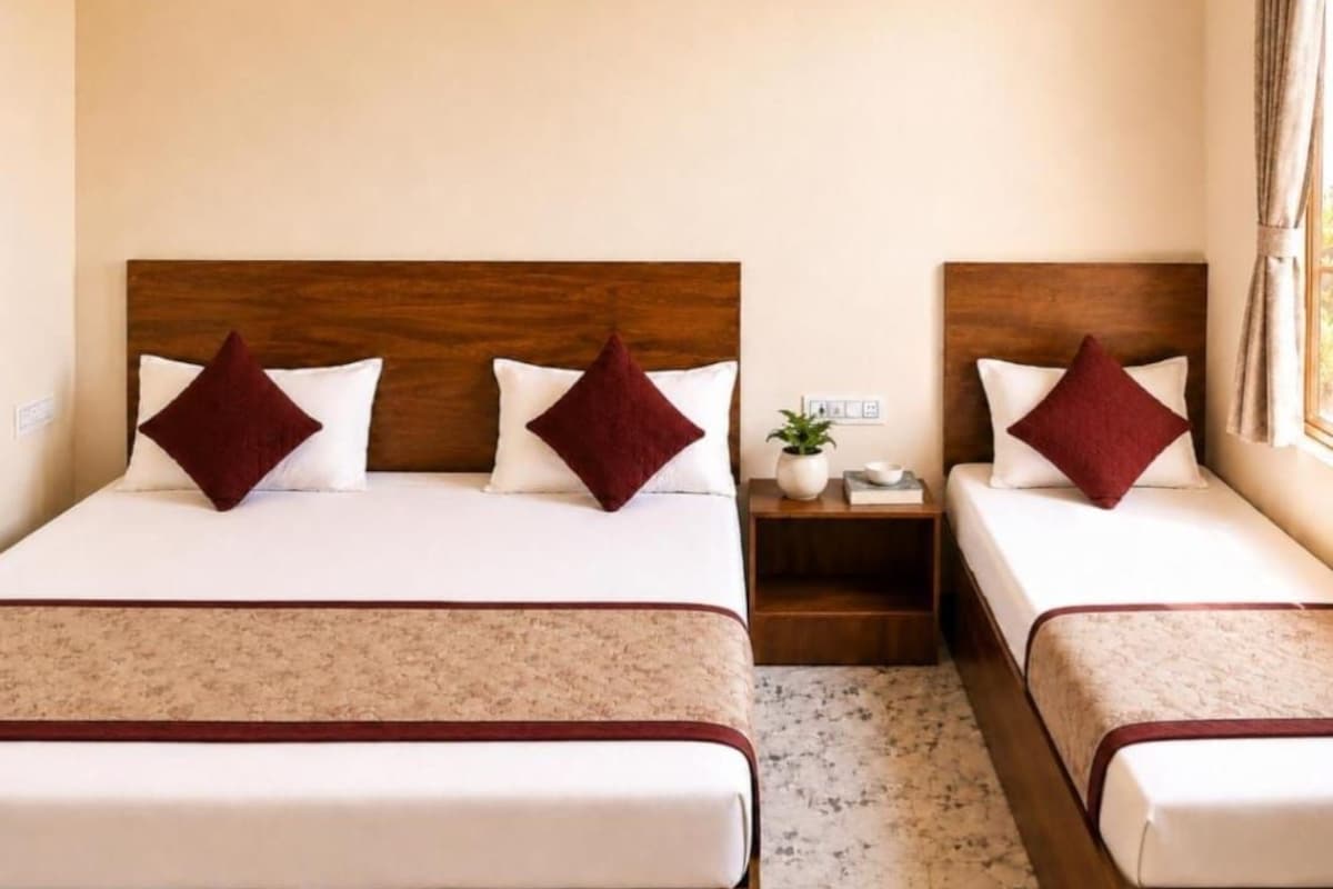 A hotel room with two beds, each with a wooden headboard, white bedding, and a red accent pillow.