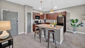 A modern kitchen with wooden cabinets, a central island with stools, and pendant lighting. - Wooded Views | King Bed | No Stairs (West Des Moines)