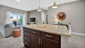 A modern kitchen with a granite countertop, dark cabinetry, and pendant lighting. - Wooded Views | King Bed | No Stairs (West Des Moines)