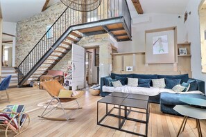 A spacious living room with a wooden floor, a blue sofa, a rocking chair, and a staircase leading to an upper level. - Pierres – A charming home where stone, light, and the good life come togeth (Saint-Cyr-au-Mont-d'Or)