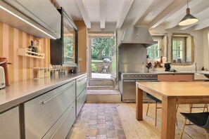 A modern kitchen with stainless steel appliances, a wooden dining table, and a view of the outdoors. - Pierres – A charming home where stone, light, and the good life come togeth (Saint-Cyr-au-Mont-d'Or)