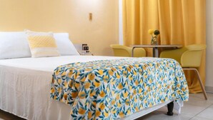 Une chambre d’hôtel avec un lit, une petite table, une chaise et un rideau jaune.