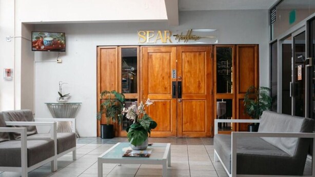 Un hall d’hôtel comprenant un comptoir d’accueil, un espace salon et des portes en bois portant l’inscription « SEAR ».