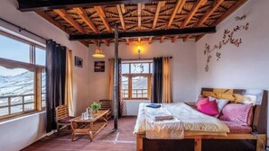 Una habitación con techo de madera, cama con ropa de cama estampada, mesa con sillas y vistas a un paisaje nevado a través de amplios ventanales.