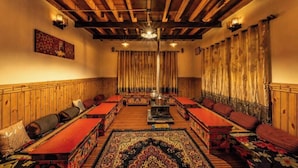 Una habitación tradicional con vigas de madera, chimenea en el centro y alfombras con diseños.