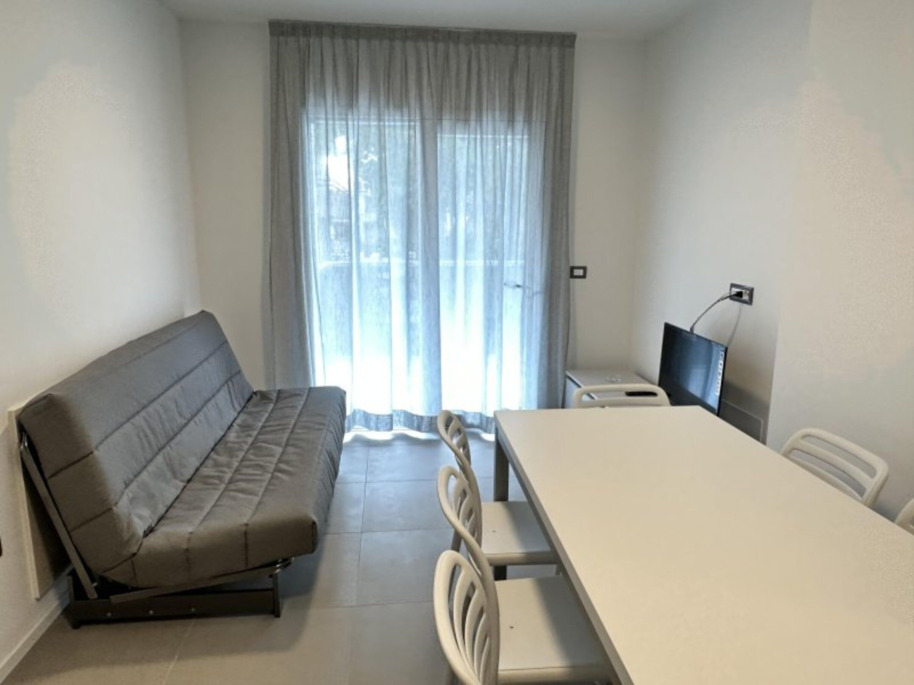 A room with a sofa, a dining table, chairs, a TV, and a window with curtains.