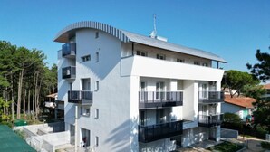 Ein modernes, mehrstöckiges Gebäude mit Balkonen, einer flachen Dachterrasse und einem kleinen Innenhof.