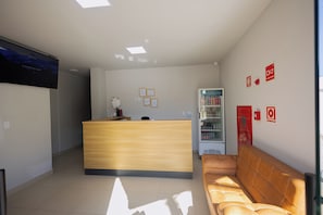 A reception area with a wooden desk, a couch, a refrigerator, and a TV on the wall.