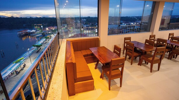 A balcony with a wooden bench and table, large windows with a city view, and a railing. - Hotel Madalena - Beiro Rio (Sao Miguel Do Guama)