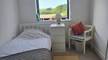 Une chambre à coucher avec un lit, un bureau, une chaise, une fenêtre donnant sur un beau paysage et un tapis.