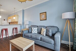 A living room with a grey sofa, wooden coffee table, red stools, a lamp, and a kitchen area in the background. - Pool View 1BR + Beach Access + Dog Friendly (Myrtle Beach)