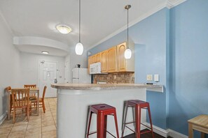 A kitchen with wooden cabinets, a white refrigerator, a microwave, and a granite countertop island with two red stools.