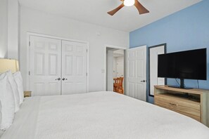 A bedroom with a bed, a ceiling fan, a TV on a wooden stand, and white double doors.