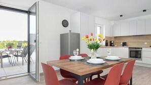 Una cocina moderna con armarios blancos, horno integrado y comedor con mesa de madera y sillas rojas.