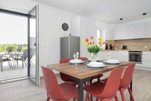 Eine moderne Küche mit weißen Schränken, einem eingebauten Backofen und einem Essbereich mit einem Holztisch und roten Stühlen.