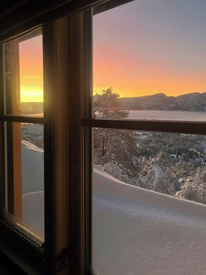 Vista dalla finestra su un paesaggio innevato con il tramonto.